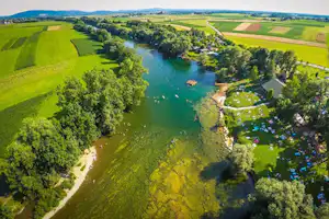 Fluss im Grünen mit Uferweg und Campingplatz am Rand, Wiesen und Felder bis zum Horizont.