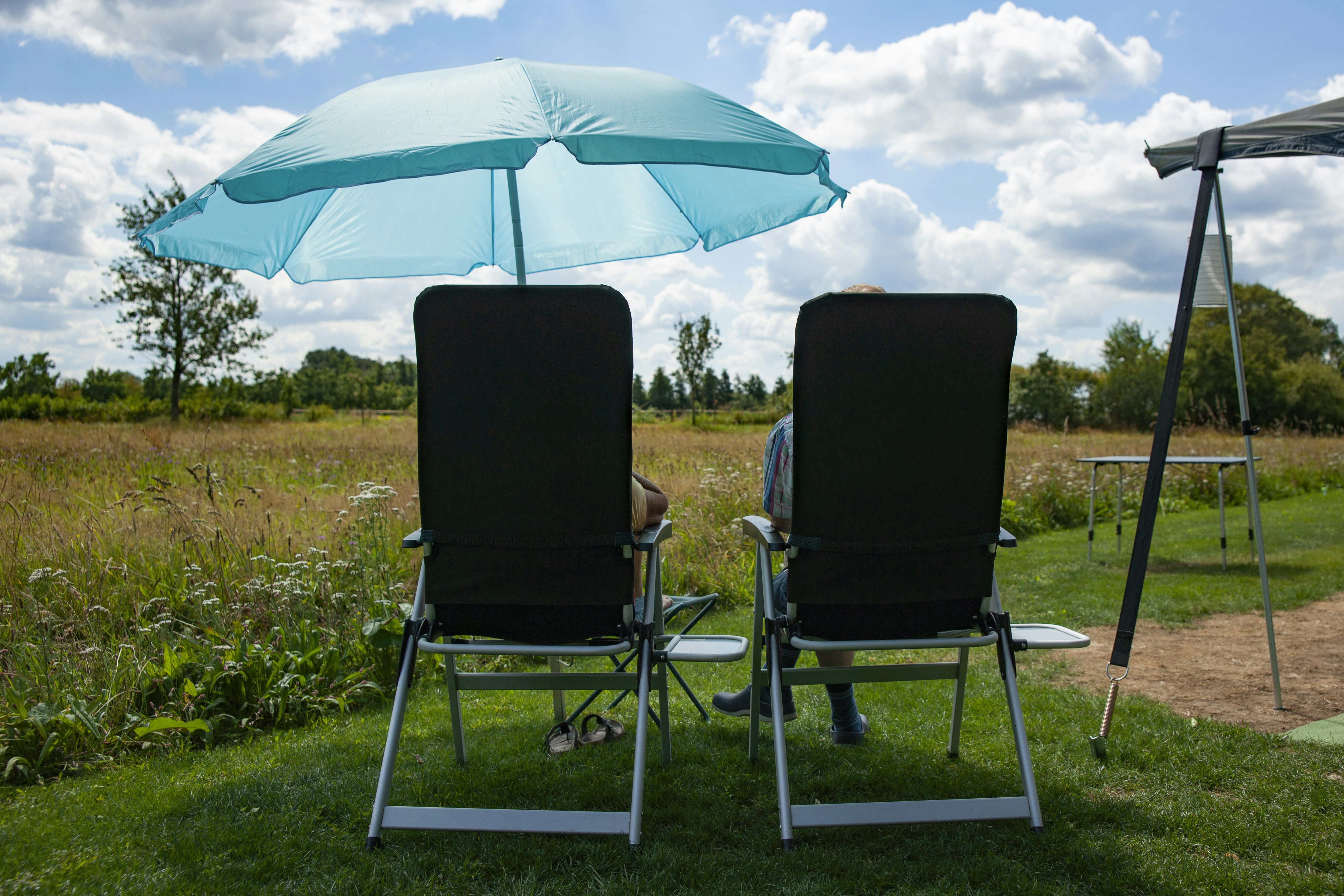 Camping Poelhuis - Camper entspannen auf Campingstühlen unter einem Sonnenschirm