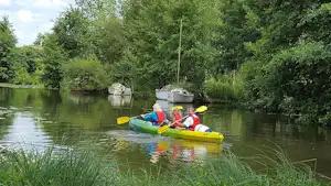 Gelbes Kajak mit zwei Personen auf einem See, umgeben von Schilf und Bäumen am Ufer.