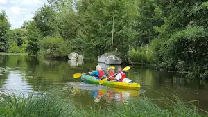 Gelbes Kajak mit zwei Personen auf einem See, umgeben von Schilf und Bäumen am Ufer.
