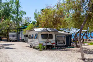 Wohnmobil auf einem Stellplatz im Campingplatz, mit Vorzelt, Holzsteg und Bäumen im Hintergrund.