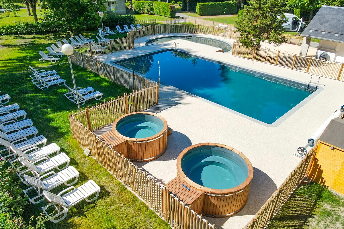 Großer Pool mit zwei runden Whirlpool-Becken, Holzfassungen und Liegestühlen im Garten eines Campingplatzes.