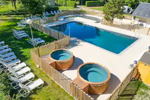Großer Pool mit zwei runden Whirlpool-Becken, Holzfassungen und Liegestühlen im Garten eines Campingplatzes.