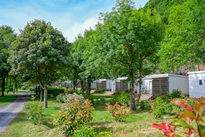 Campingplatz mit Wohnwagen und Mobilheimen, gepflasterter Straße und gepflegtem Grün mit Bäumen und Sträuchern im Vordergrund.