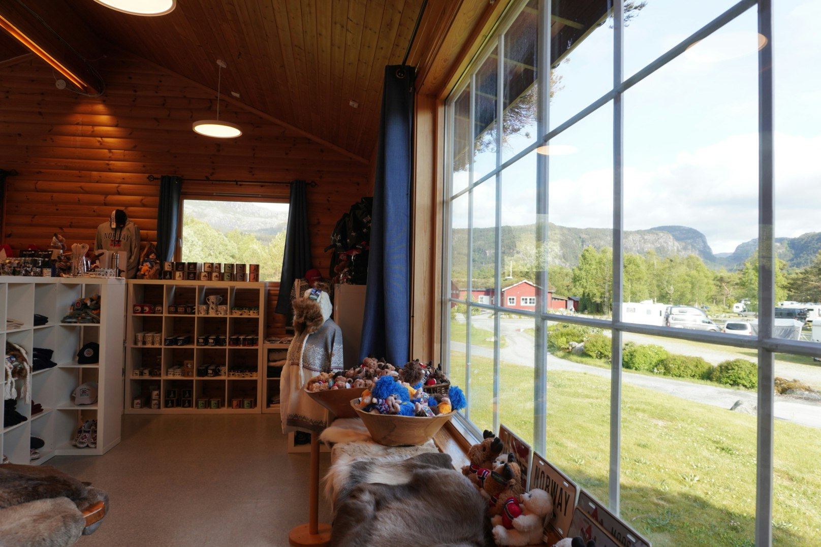 Innenraum eines Campinghauses mit Holzdecke, großen Fenstern und Blick ins Tal; Tisch mit Spielzeug und Haustieren im Vordergrund.