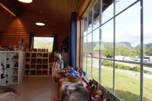 Innenraum eines Campinghauses mit Holzdecke, großen Fenstern und Blick ins Tal; Tisch mit Spielzeug und Haustieren im Vordergrund.
