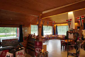 Innenraum einer Blockhütte im Campingbereich mit Holzwänden, Tischen, Stühlen und mehreren Flaggen an der Wand.