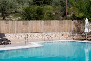 Campingpool mit Leiter, Sonnenliegen und Sonnenschirm auf der Terrasse, umgeben von Steinmauer und Holzsichtschutz, im Grünen.