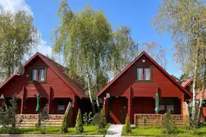 Zwei rote Holzferienhäuser mit grünen Fensterläden, Türen und Veranda, umgeben von Birken und grünem Rasen.