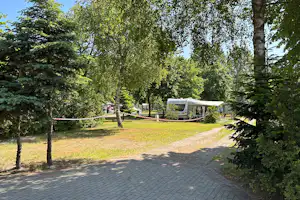 Wohnmobil auf einem Stellplatz im Grünen, mit Vorzelt, Stühlen und gepflastertem Weg zwischen Bäumen.
