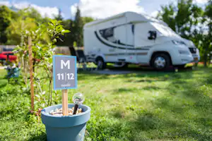 Schild mit Platznummer am Campingplatz, im Hintergrund ein Wohnmobil auf dem Stellplatz und grüner Rasen mit Bäumen.