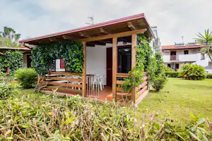 Holzveranda am Bungalow mit Sitzgarnitur, umrankt von Kletterpflanzen, im gepflegten Garten mit Rasen und Hecken.