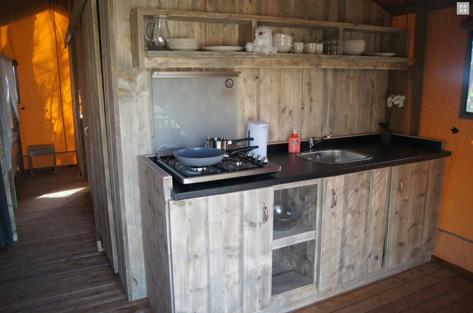 Holz-Küchenzeile im Campingbereich mit Herd, Spüle, Töpfen und Gewürzregal im Innenraum.