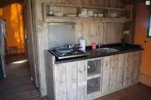 Holz-Küchenzeile im Campingbereich mit Herd, Spüle, Töpfen und Gewürzregal im Innenraum.
