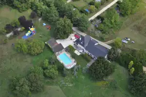 Luftaufnahme eines Campingplatzes mit Pool, mehreren Gebäuden, Stellplätzen und Wegen im Grünen.