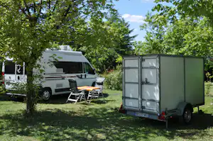 Wohnmobil und Anhänger auf einer Campingwiese, mit Gartenstühlen und Bäumen im Hintergrund.