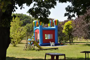 Aufblasbares Hüpfburg-Spielgerät mit Rutsche im grünen Campinggarten, umgeben von Bäumen und Wiese.