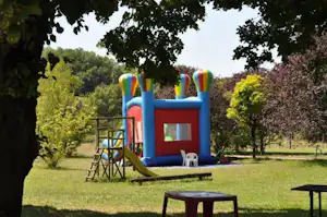 Buntes Hüpfburg-Spielgerät im Campinggarten, umgeben von Rasen, Bäumen und einem Tisch mit Stühlen.