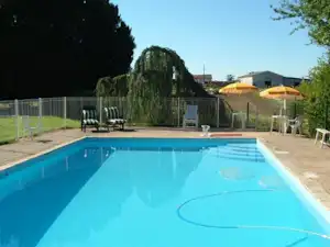 Camping-Pool mit Sonnenschirmen, Liegestühlen und Zaun im Hintergrund, daneben Wege und Gebäude.