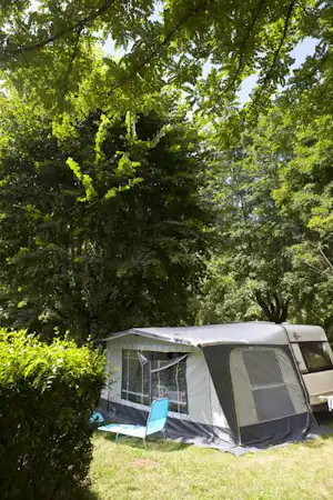 Zelt am Campingplatz im Grünen, umgeben von Bäumen, mit Vorzelt und Rasenfläche im Vordergrund.