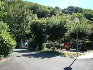 Spielplatz mit Rutsche und Klettergerüst auf einem Campingplatz, umgeben von Bäumen und Hecken.