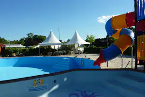Blauer Camping-Pool mit Kinder-Rutsche im Vordergrund, im Hintergrund weiße Zelte und Bäume unter klarem Himmel.