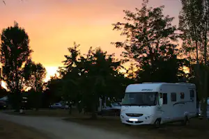 Weißes Wohnmobil steht auf dem Campingplatz am Weg, umgeben von Bäumen, bei Sonnenuntergang.