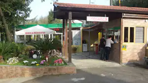 Rezeption am Campingplatz mit Überdachung, Schild „RECEPTION“, Blumenbeet und Sitzgelegenheiten im Eingangsbereich.