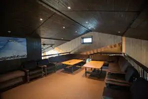 Wohnbereich in einer Holz-Campinghütte mit Sitzbänken, Couchtisch und Polsterbank entlang der Seitenwände.