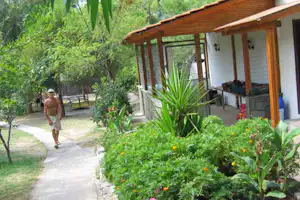 Bungalow mit Holzveranda und Sitzbank, umgeben von Blumenbeeten und Wegen im grünen Campinggarten.