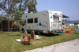 Wohnmobil auf dem Stellplatz mit Tisch und Stühlen auf dem Rasen, Bäume im Hintergrund und Zelt am Rand.