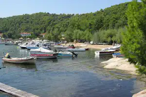 Bootshafen am Ufer mit vielen Booten, Stegen und einem Weg am Wasser, umgeben von grünen Hügeln.