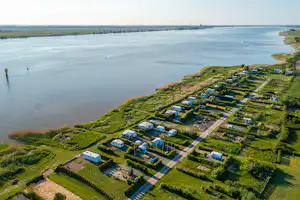 Campingplatz am Fluss mit vielen Stellplätzen, kleinen Wohnwagen und Wegen auf der grünen Wiese.