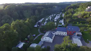 Luftaufnahme einer Campinganlage im grünen Tal mit Reihen von Stellplätzen, Gebäuden und umgebenden Wäldern.