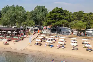 Camping Residence Punta Spin - Strand des Mittelmeeres mit Liegestühlen und Sonnenschirmen, im Hintergrund sind Stellplätze des Campingplatzes zu sehen