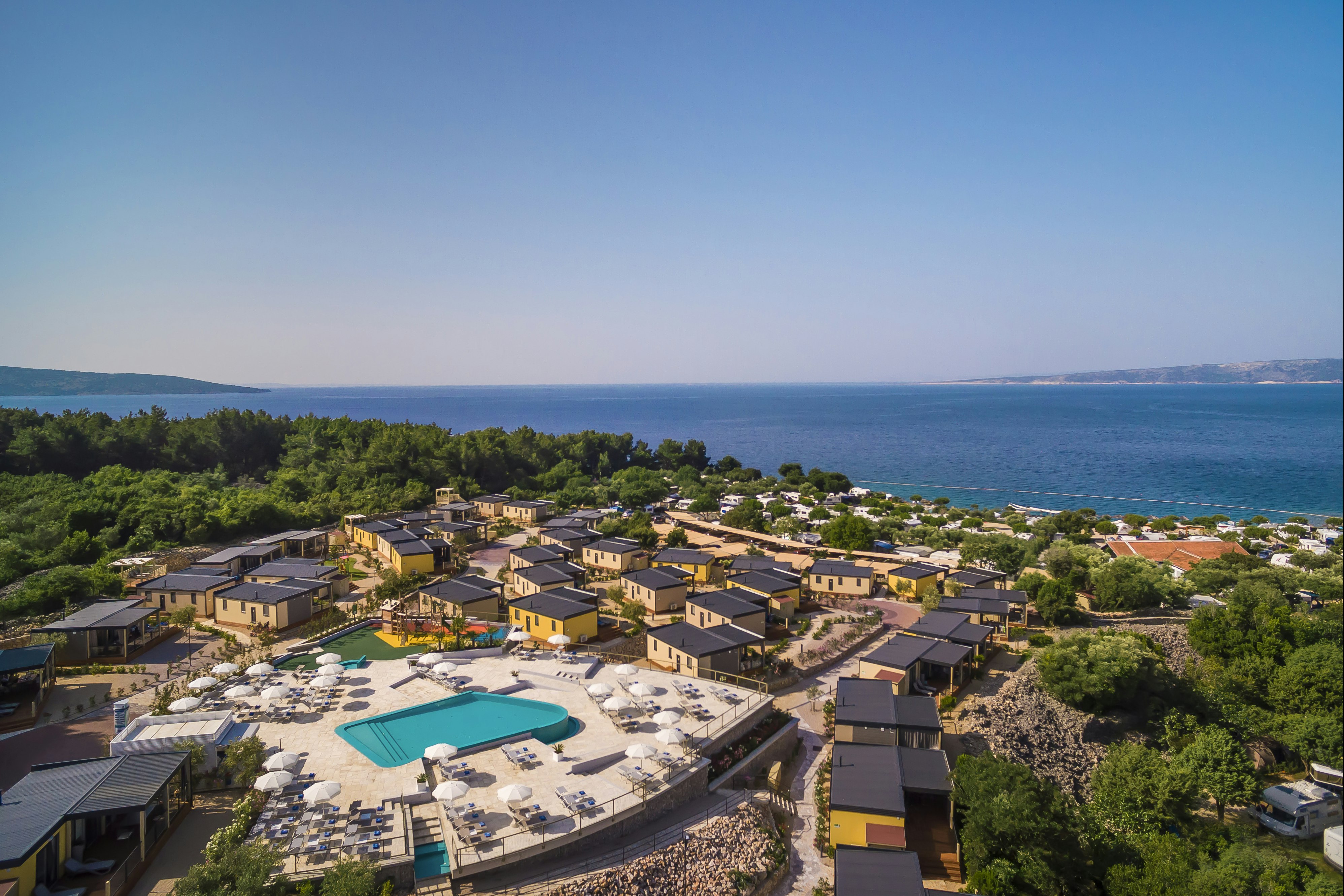 Luftaufnahme eines Campingplatzes mit Pool, Reihen von Unterkünften und Blick auf das Meer und die Küste.