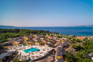 Luftaufnahme eines Campingplatzes mit Pool, Reihen von Unterkünften und Blick auf das Meer und die Küste.
