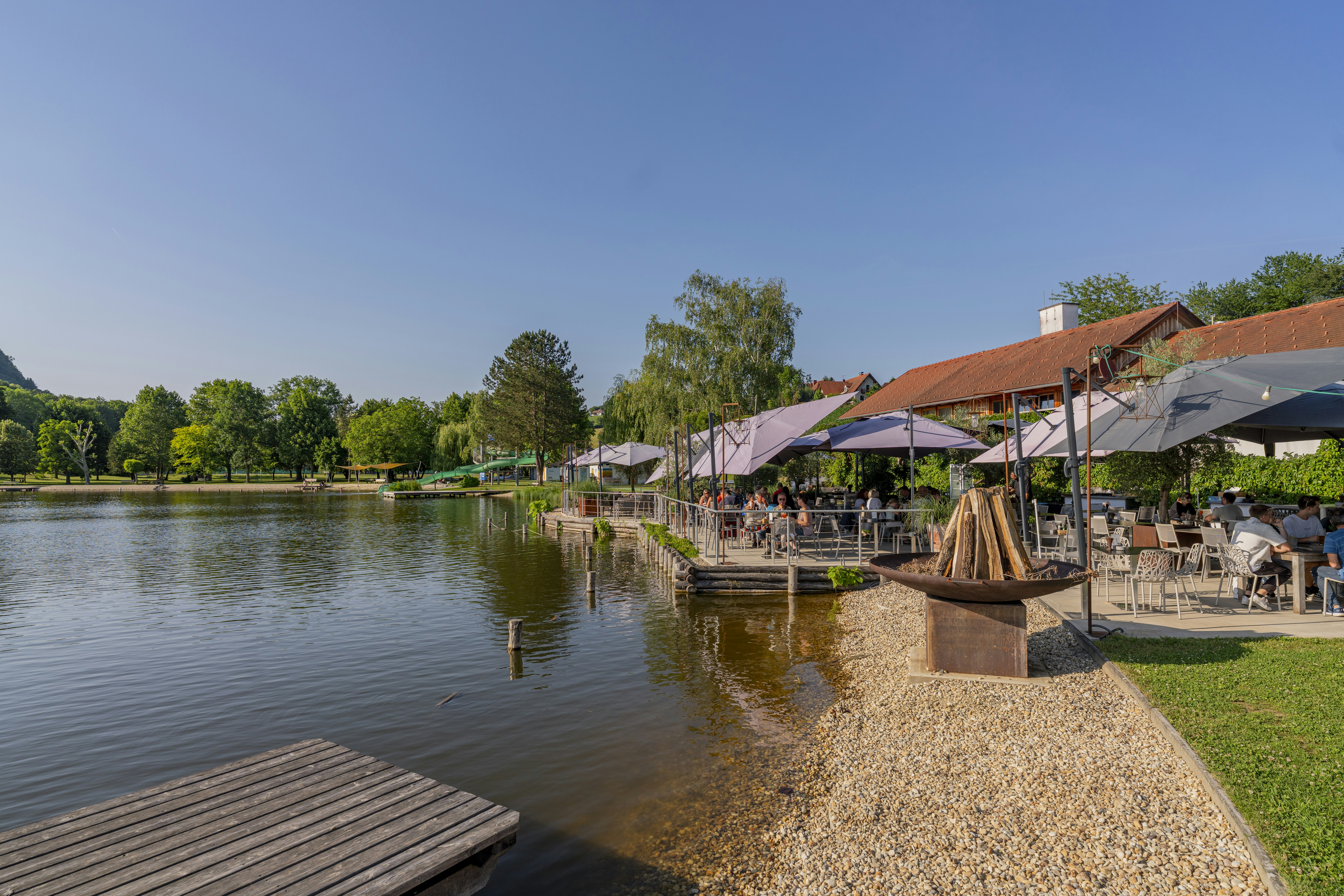 Camping Resort Riegersburg - Badesee mit Sitzgelegenheiten und Sonnenschirmen am Ufer