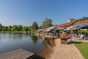 Camping Resort Riegersburg - Badesee mit Sitzgelegenheiten und Sonnenschirmen am Ufer
