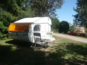 Wohnwagen mit Vorzelt, Tisch und Stühlen auf dem Stellplatz im Grünen, umgeben von Bäumen.