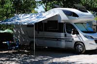 Camping Ribamar - Wohnmobil mit Vordach auf einem mit Kies ausgelegten Standplatz im Halbschatten unter Bäumen