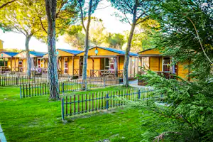 Reihe von Bungalows auf einem Campingplatz, umgeben von Rasen, Zäunen und Bäumen, mit Wegen zwischen den Unterkünften.
