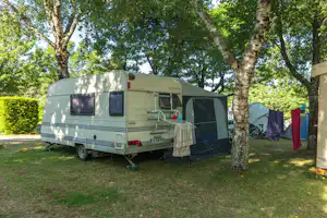 Wohnwagen auf dem Campingplatz zwischen Bäumen, mit Vorzelt und Wäscheleine im grünen Gras.