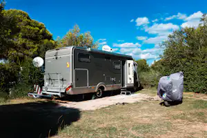 Wohnmobil auf einem Stellplatz mit Vorzelt und Markise, daneben ein großer Wäschesack, umgeben von Bäumen und Sträuchern.