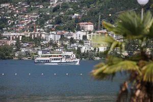 Camping Rivabella - Blick vom Campingplatz über den See Lago di Garlate auf ein Schiff und die umliegende Landschaft