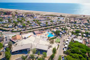 Luftaufnahme eines Campingplatzes am Meer mit Schwimmbecken, Wohnmobilen und Wegen zwischen Bäumen und Stellplätzen.