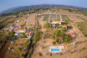 Luftaufnahme einer Campinganlage mit Wohnhäusern, orangefarbenen Dächern und einem großen Weinberg in hügeliger Landschaft.