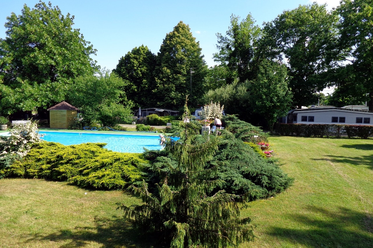Camping Romantik - Poolbereich im Grünen im Vordergrund, Stellplätze zwischen Bäumen im Hintergrund