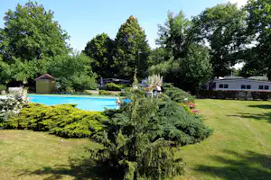 Schwimmbecken auf dem Campingplatz, gepflegte Hecken und Rasenflächen, im Hintergrund Wohnwagen und Bäume.