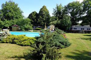 Camping Romantik - Poolbereich im Grünen im Vordergrund, Stellplätze zwischen Bäumen im Hintergrund